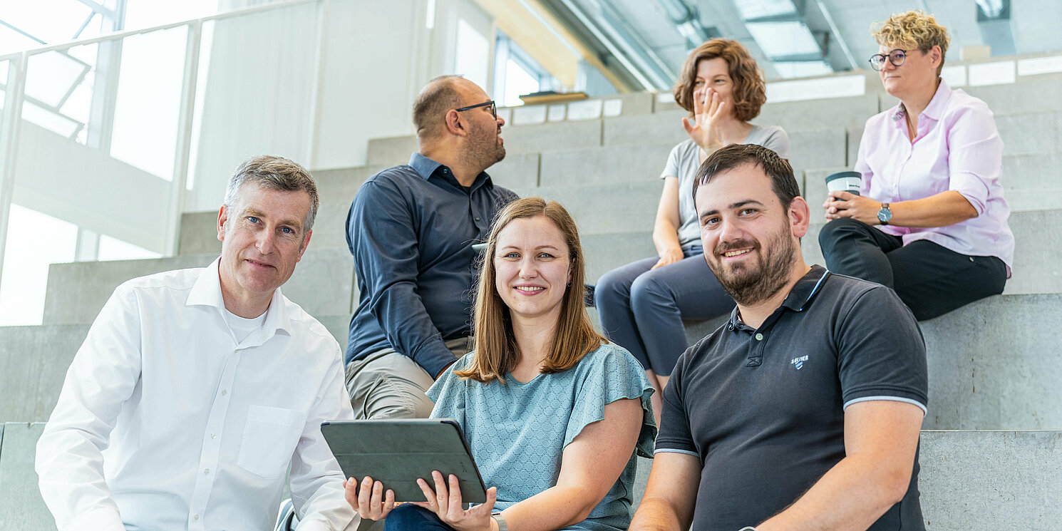 Studierende sitzen auf einer großen Treppe und unterhalten sich mit ihrem Dozenten.