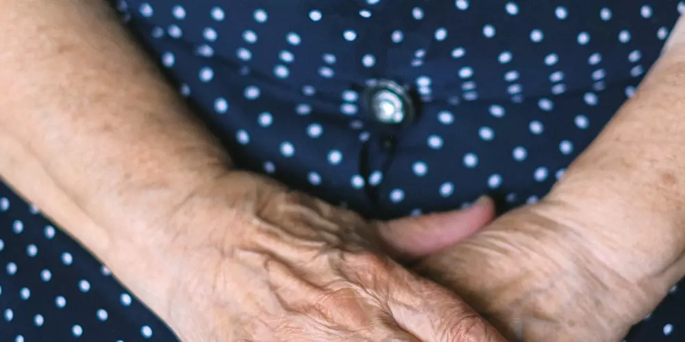 Hintergrund: Blaues Kleid mit weißen Punkten. Alte Hände liegen gefaltet darauf.