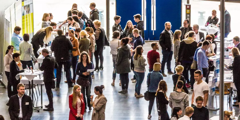 Foyer mit Messe-Ständen und vielen interessierten Besucher:innen 