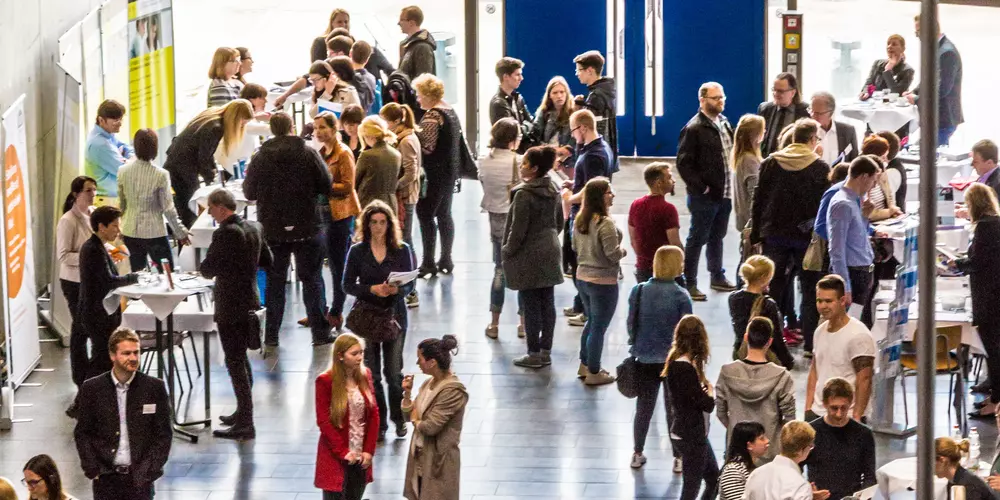 Foyer mit Messe-Ständen und vielen interessierten Besucher:innen 