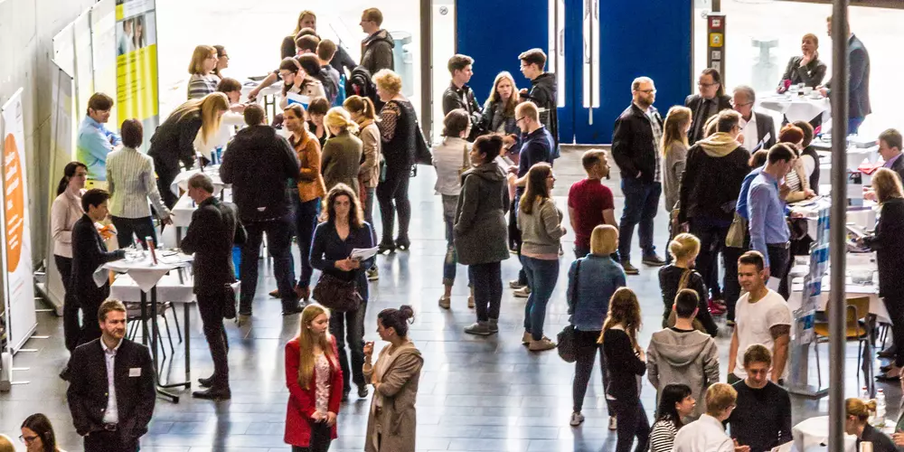 Foyer mit Messe-Ständen und vielen interessierten Besucher:innen 