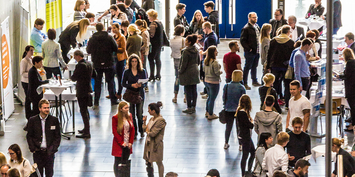 Foyer mit Messe-Ständen und vielen interessierten Besucher:innen 