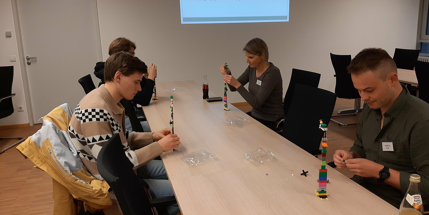 Studierende sitzen um einen Tisch und basteln Lego 