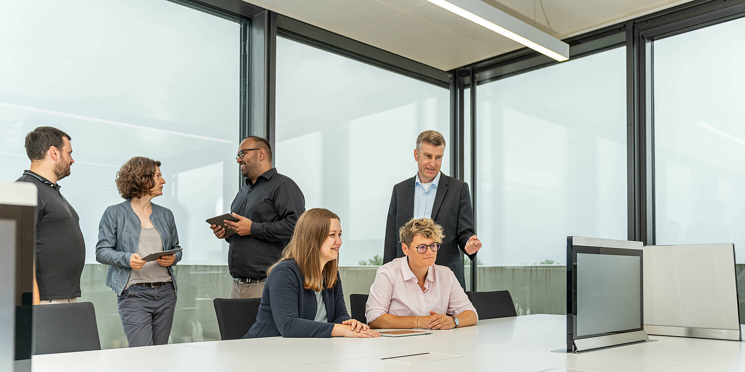 Studierende und ihr Dozent arbeiten und besprechen sich in einem Seminarraum. 