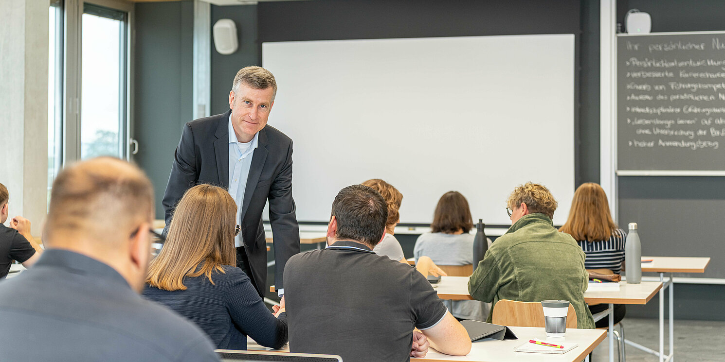 Leitung und Kommunikationsmanagement berufsbegleitend studieren Studierende lernen mit ihrem Dozenten in einem Seminarraum.