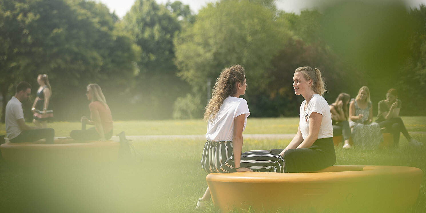 Gruppen von Studierenden sitzen draußen auf der OTH Wiese auf orangen Sitzkreisen.