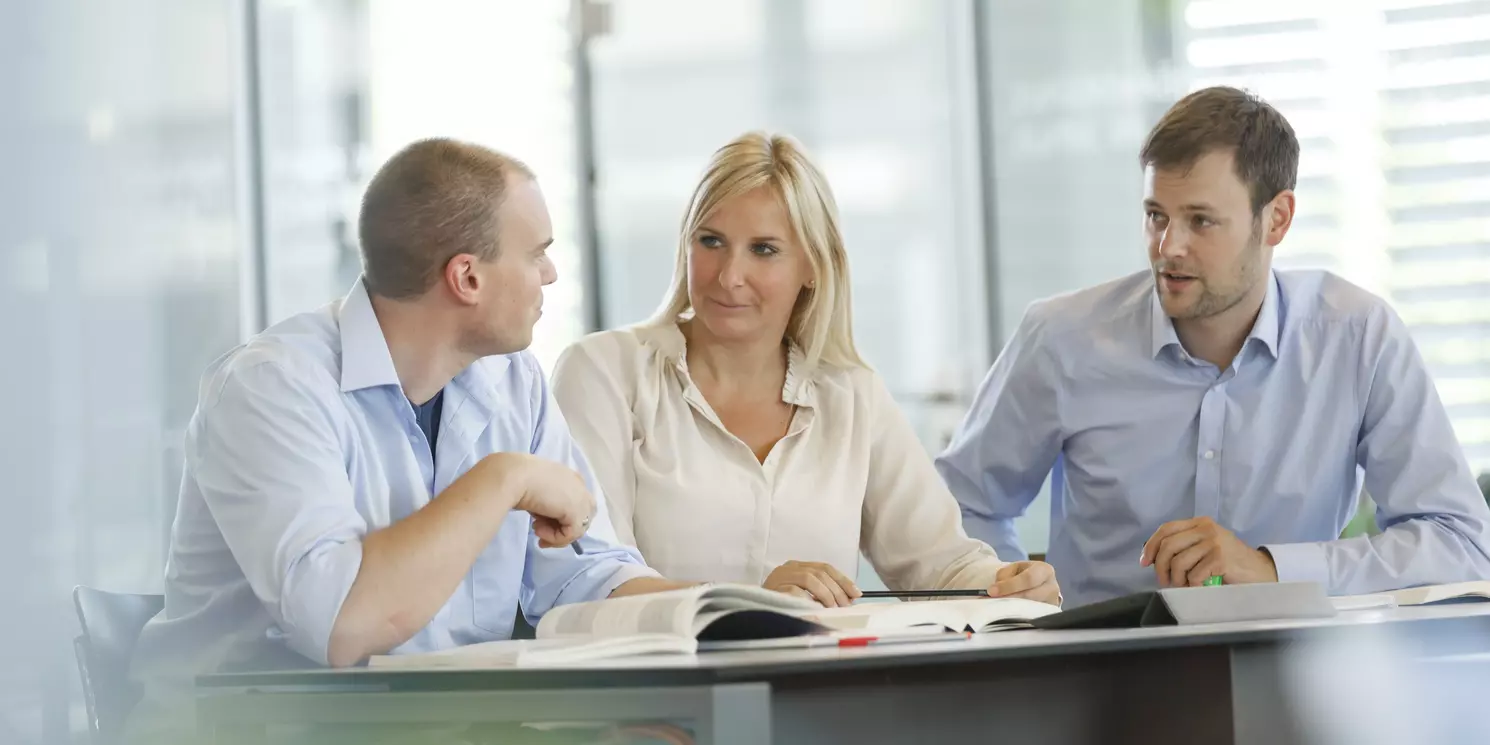 Hochschulzertifikat Certified Conflict Practitioner berufsbegleitend absolvieren Drei Studierende lernen und arbeiten an einem Tisch mit Büchern und Unterlagen