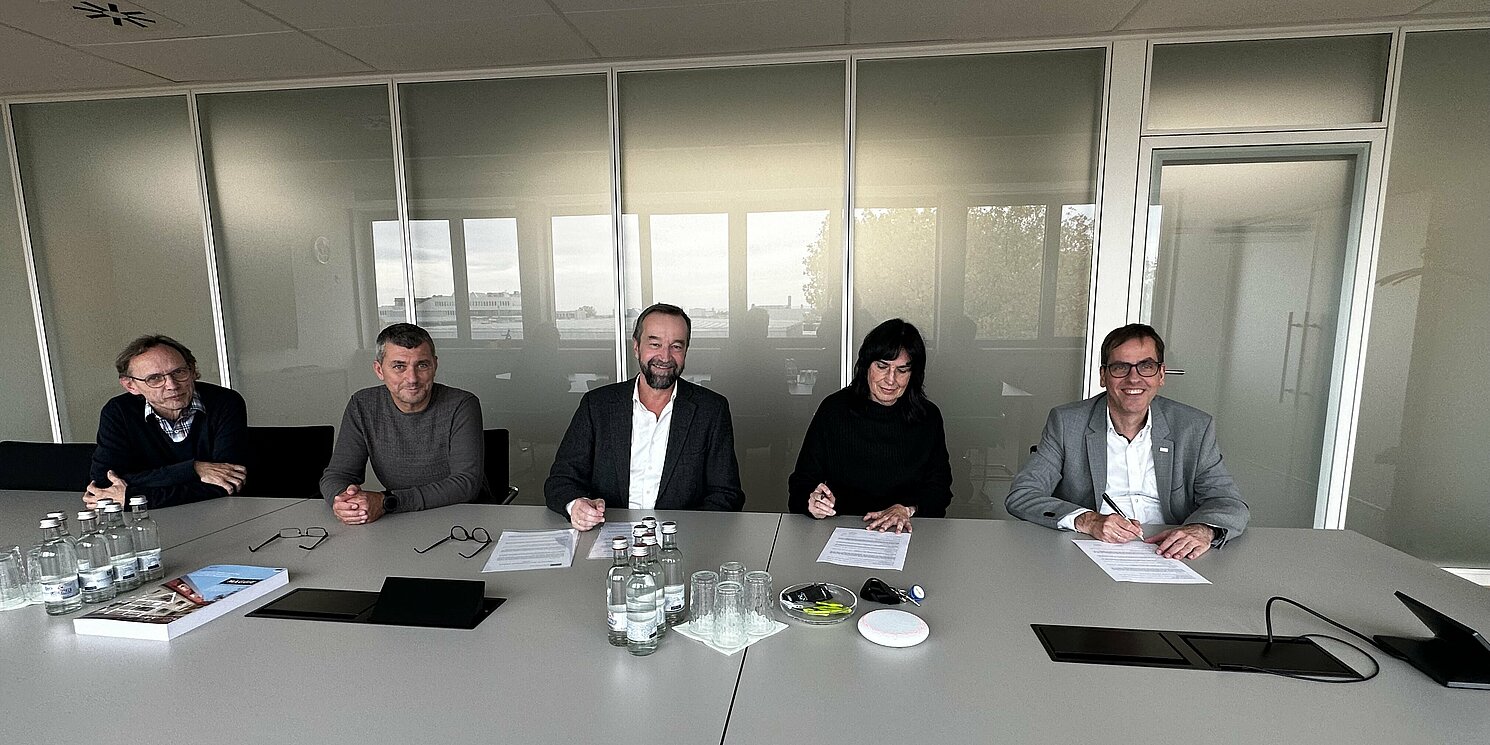 5 Personen sitzen an einem Tisch und unterschreiben Dokumente