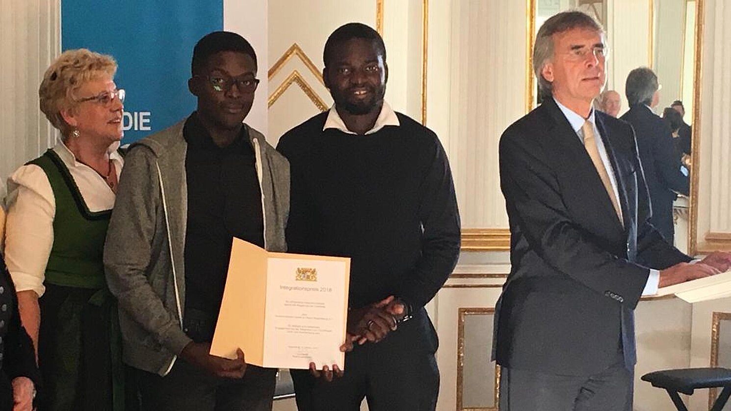 Kevin Tchokodeu (Vorsitzender ACAR e. V.; 2. von links) und Romuald Pevoubou (Kassenprüfer; 3. von links), die sich über ihre Urkunde freuen, und der Präsident der Regierung der Oberpfalz Axel Bartelt (ganz rechts im Bild). 