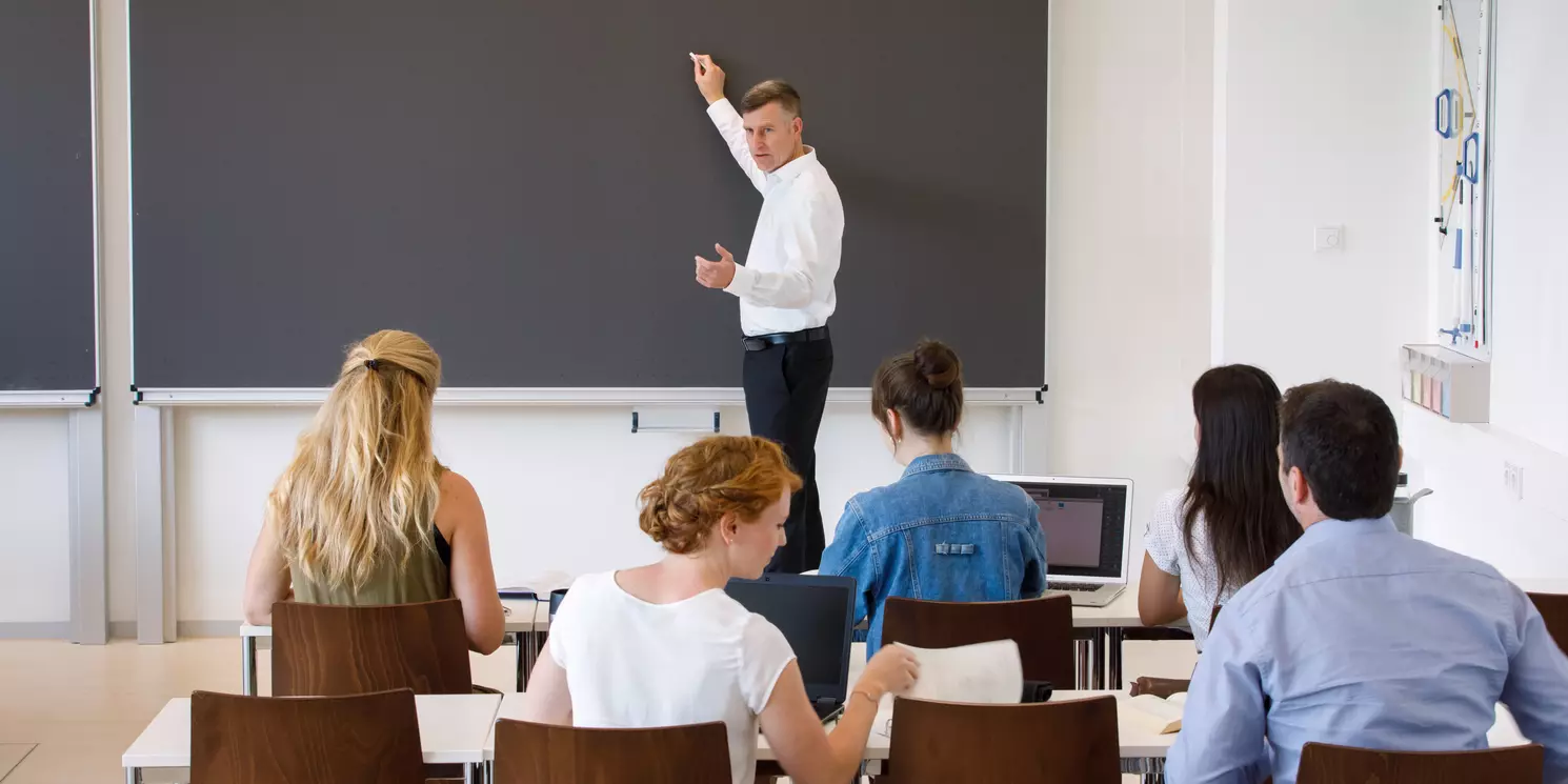 Professor mit fünf Studierenden in einem Seminarraum