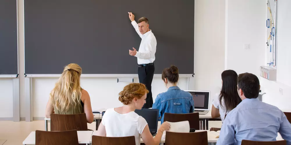 Professor mit fünf Studierenden in einem Seminarraum