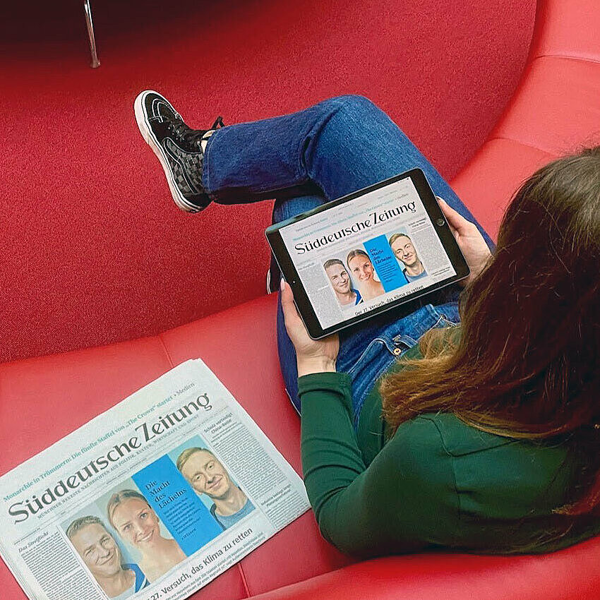 Studentin liest eine Online-Zeitung auf einem roten Sofa