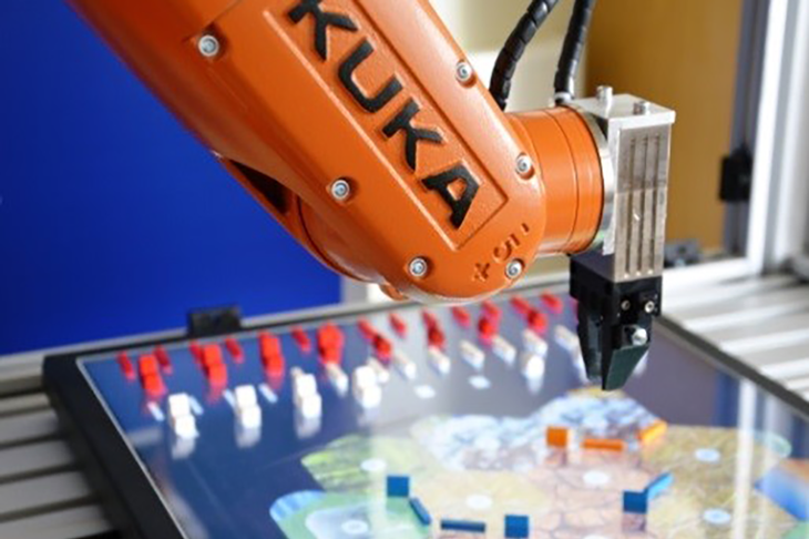 Präzise setzt der Kleinroboter Straßen und Gebäude auf das Bildschirm-Spielbrett von Siedler von Catan. Bild: KUKA Robotics. 