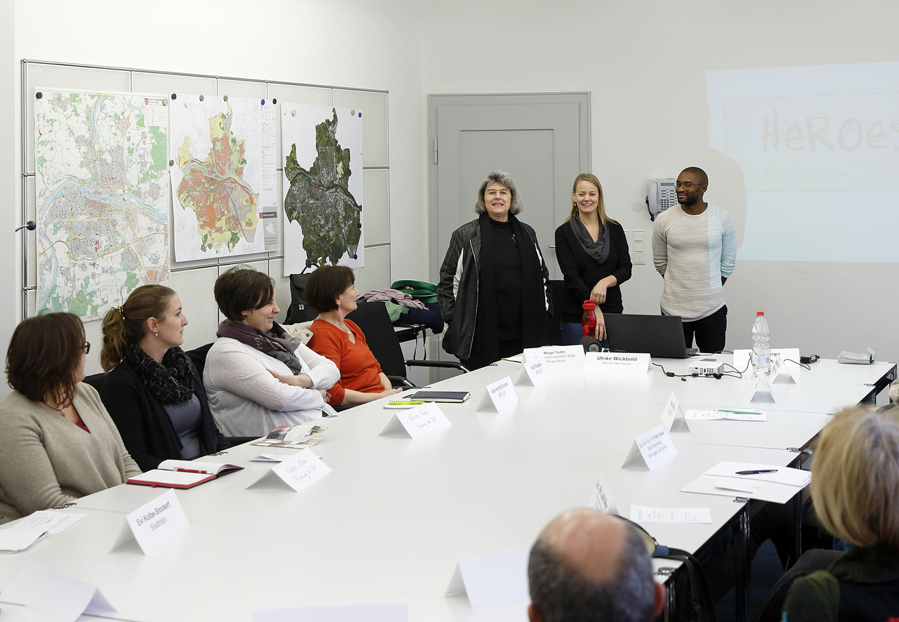 Marga Teufel (stehend links), Leiterin der Gleichstellungsstelle der Stadt Regensburg, begrüßt (stehend von links) Ulrike Wickbold und Eric Mbarga vom Nürnberger Projekt „Heroes“.